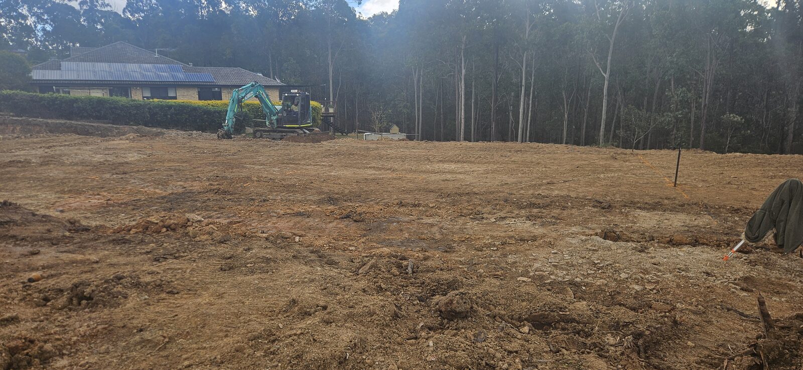 Sollid Solutions excavator working on a cleared block preparing the ground, house and forest behind
