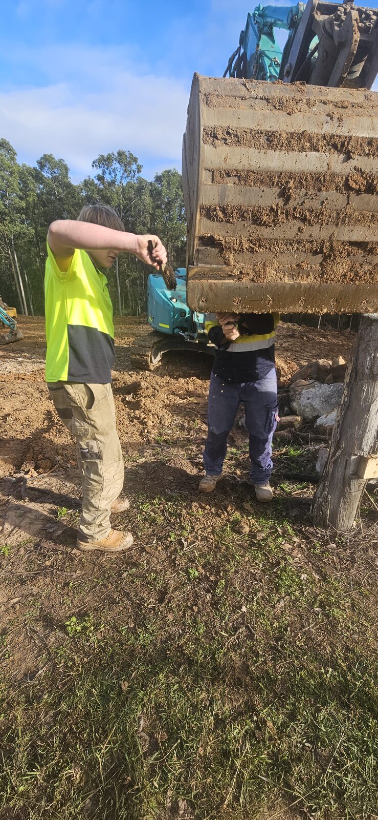 Father and son working together under the raised excavator bucket