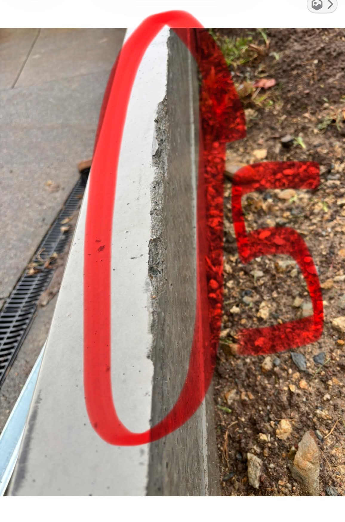 Close-up of a cracked and spalling concrete edge on the retaining wall, circled in red