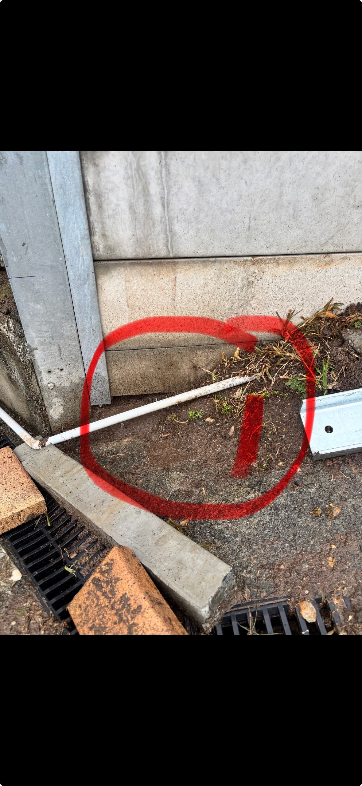 Base of retaining wall with a thin white drainage pipe and no proper drainage zone