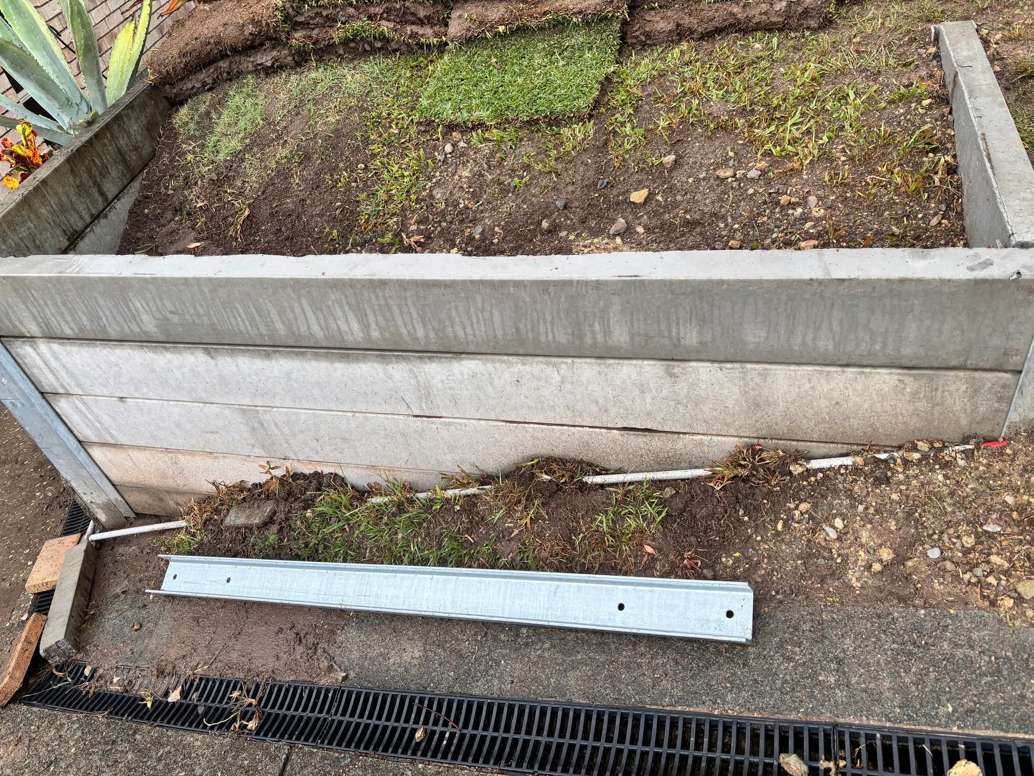 Galvanised channel bracket lying loose on the ground beside the retaining wall