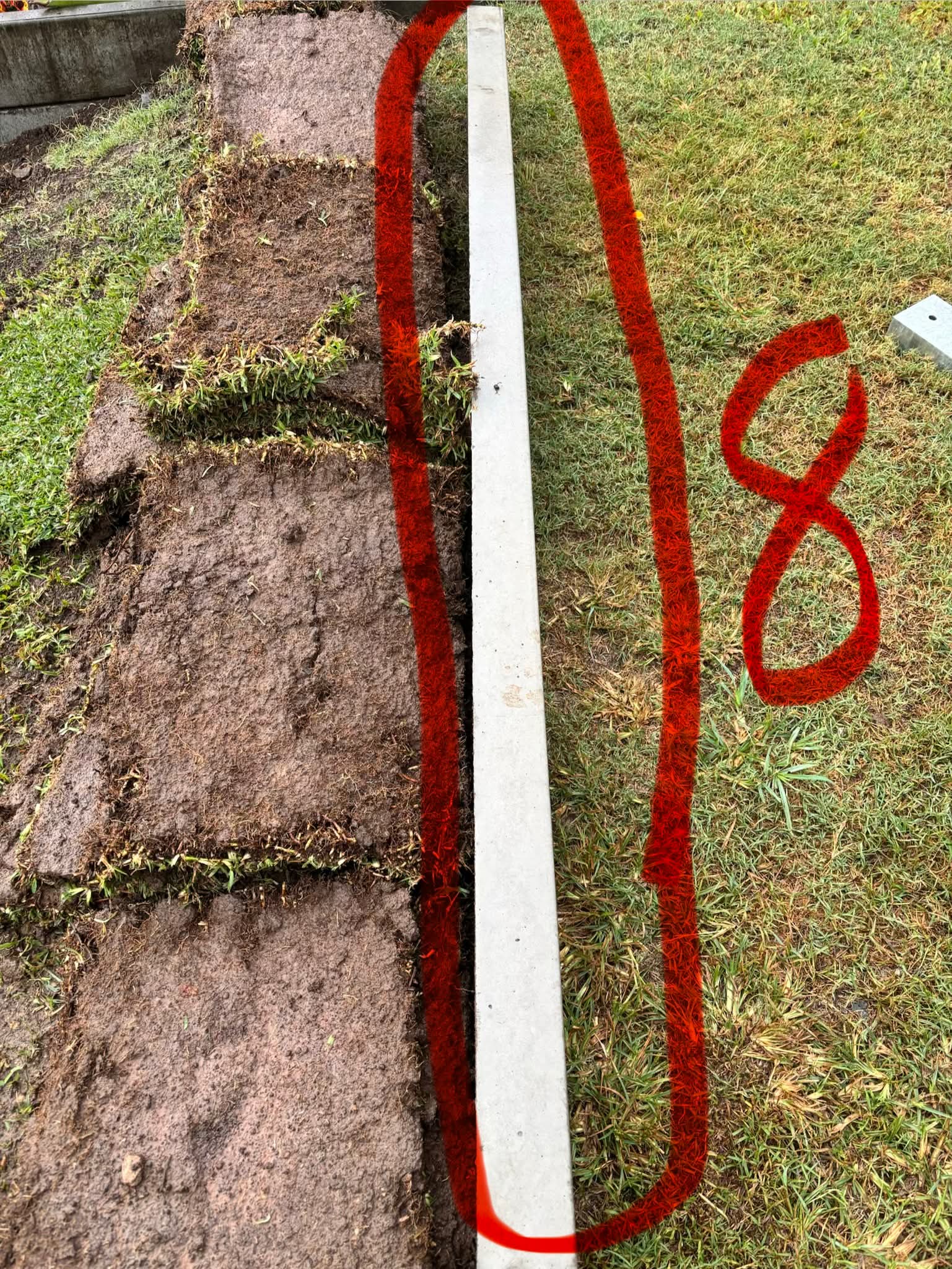 Turf peeled back behind a retaining wall revealing little to no drainage aggregate