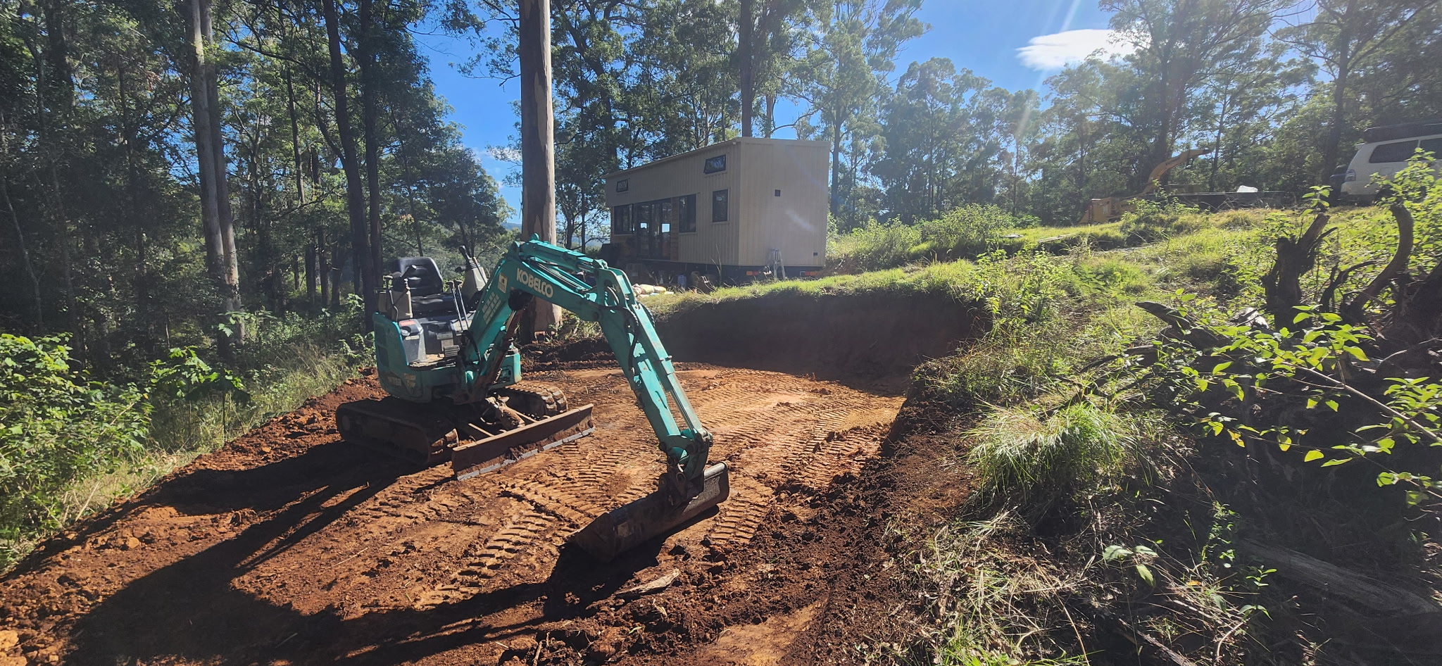 Excavator cutting a pad into a tight slope below a tiny home