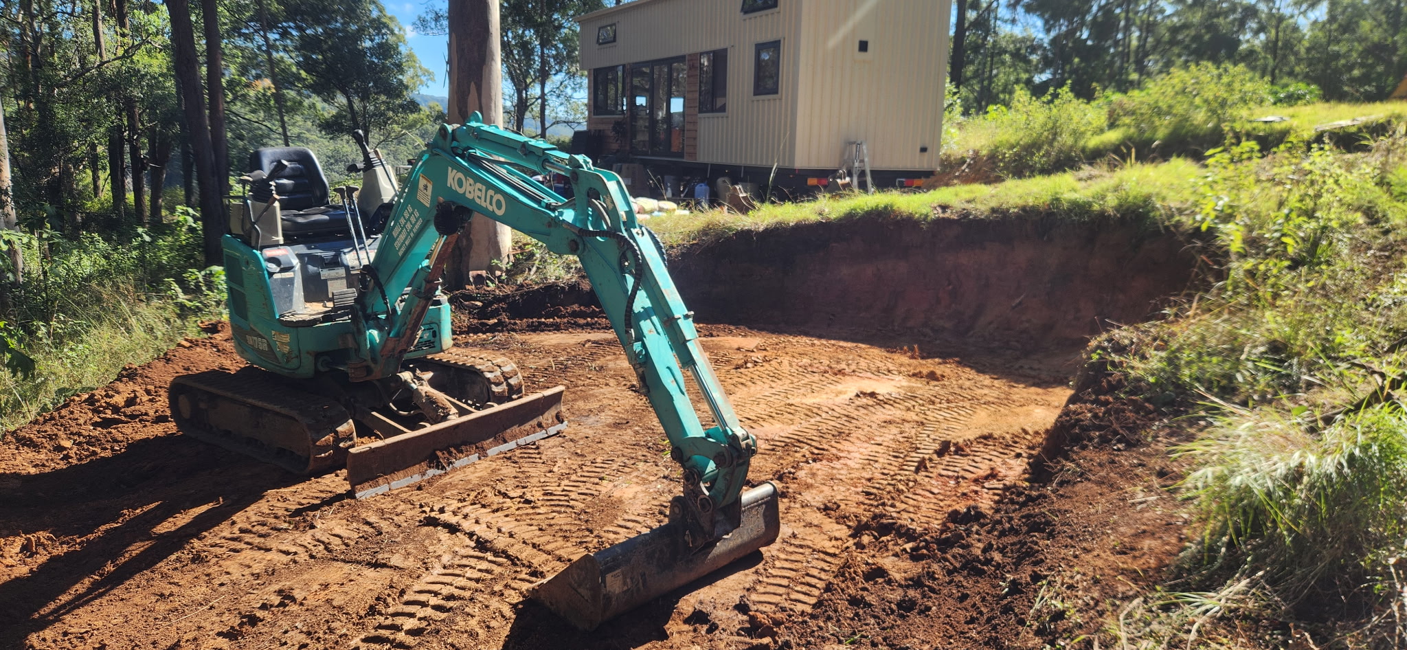 Excavator shaping and trimming a pad in a confined hinterland spot