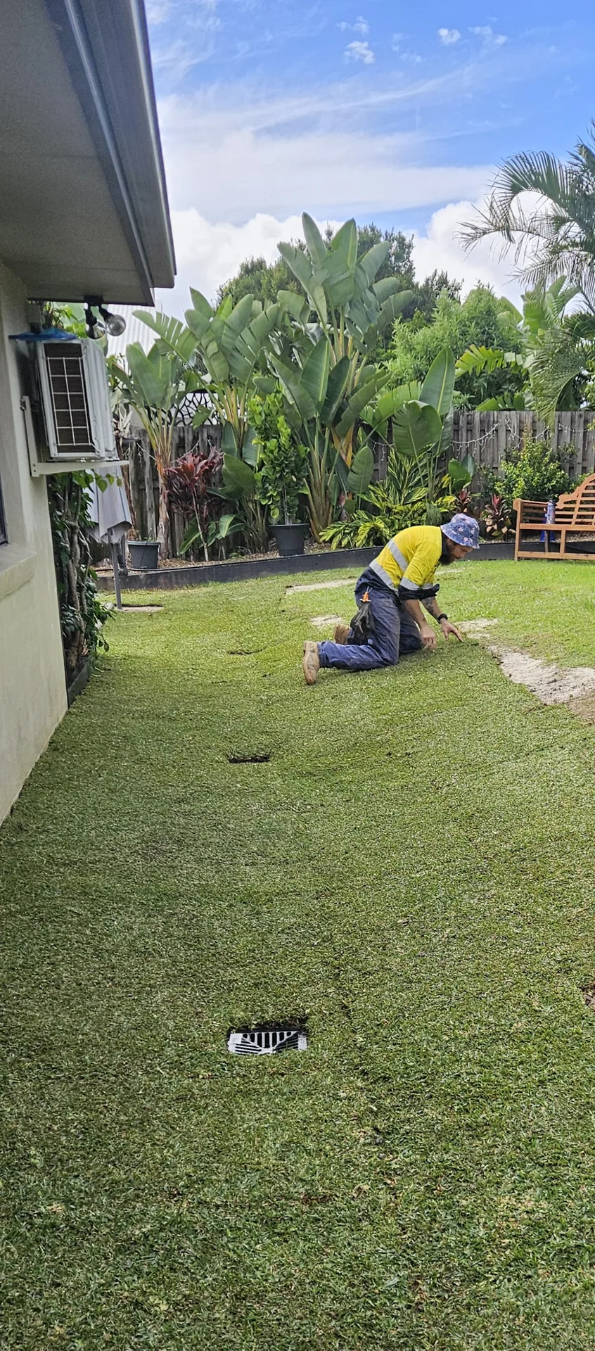 Sollid Solutions crew laying fresh turf along a Gold Coast side yard, finishing around a stormwater grate